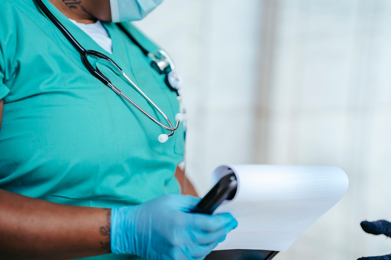 Side view of crop anonymous tattooed ethnic female medic in uniform with stethoscope and papers on clipboard