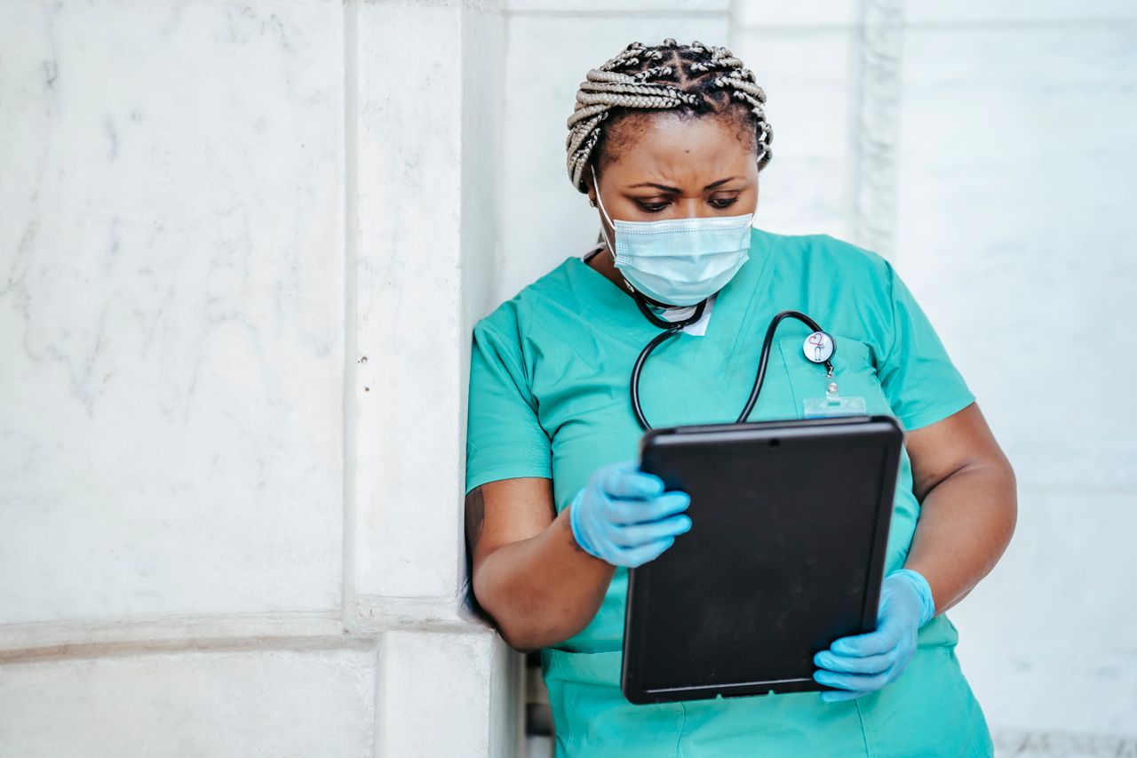 Concentrated African American female doctor in uniform and protective mask looking through documents in folder